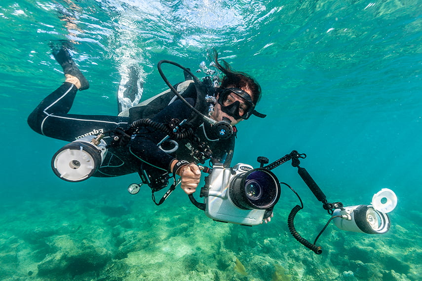 Cristina Mittermeier diving underwater while holding a underwater camera rig.