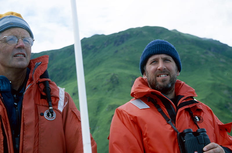 Tim Tinker and Dr. James Estes standing in front of a mountain wearing orange jackets.