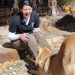 Sarah Brenkert laughing and playing with a dog.