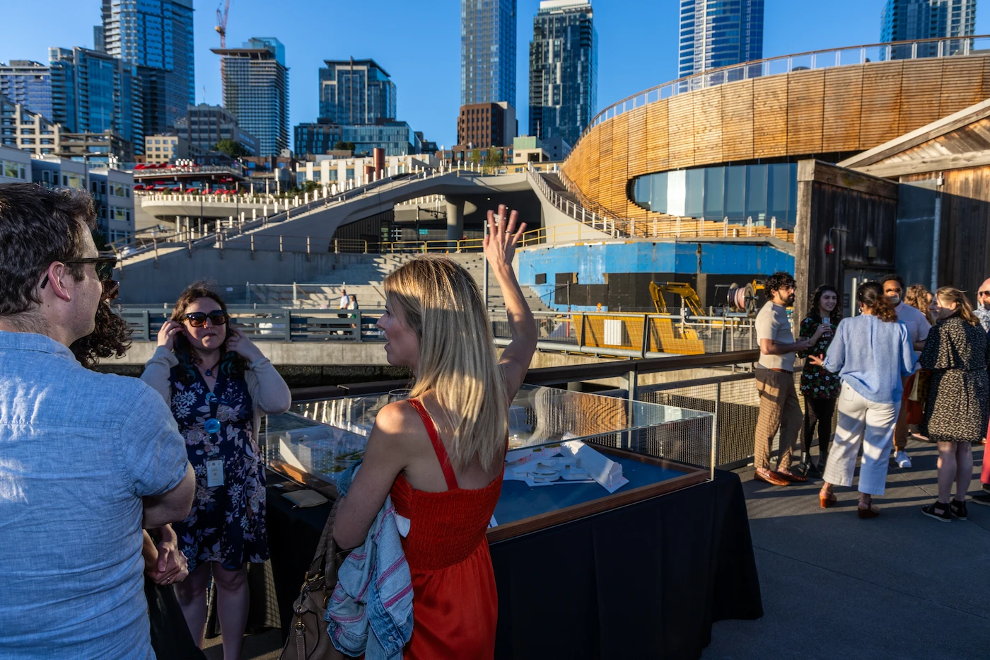 Guests at Splash in front of an architectural model of the Seattle Aquarium’s new Ocean Pavilion building, with the constructed Ocean Pavilion building in the background behind them being showcased to show how the building has become a reality.
