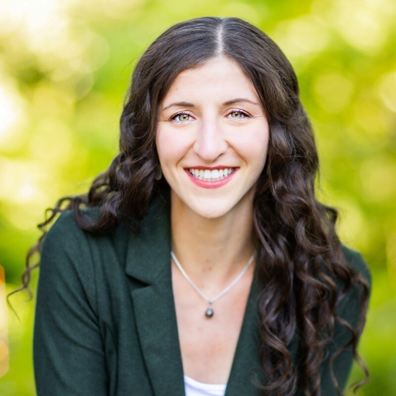 A headshot of Anja Brandon. She has long, dark curly hair.