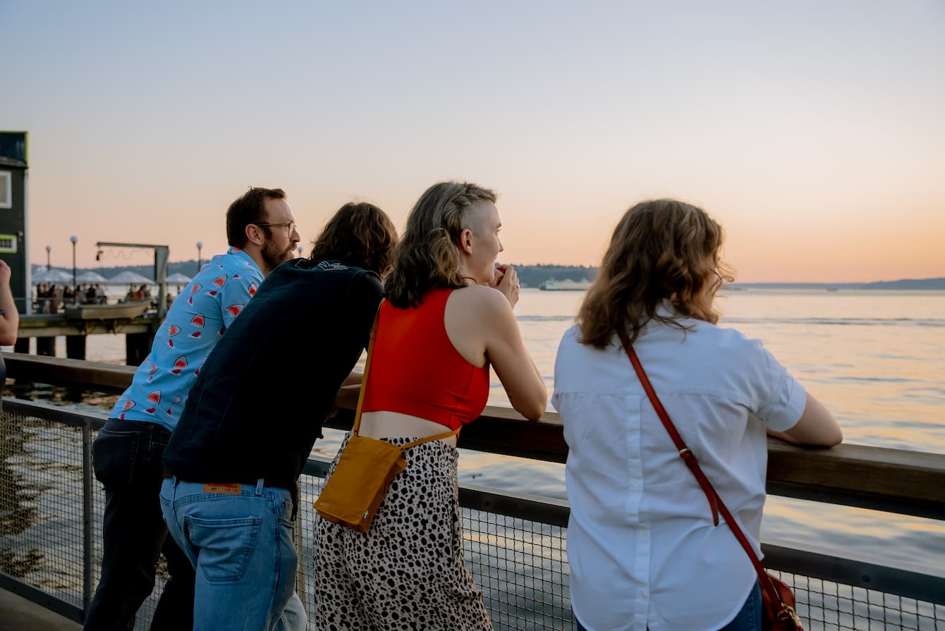 A back shot of four people leaning on a railing and gazing out onto the Salish Sea at sunset.