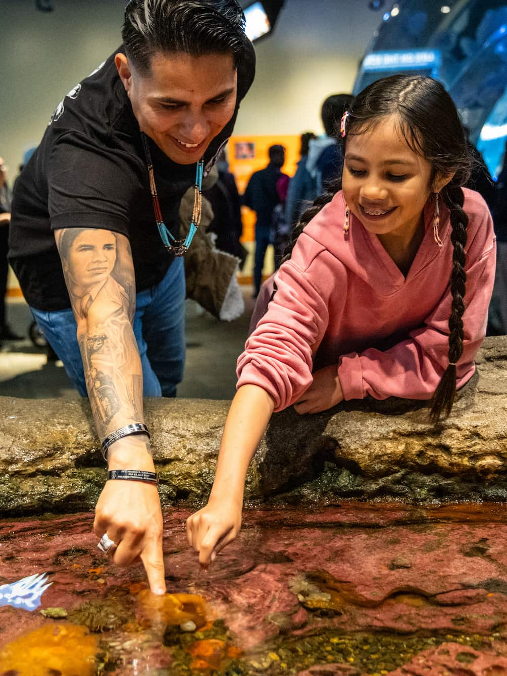 An adult and a child smiling while interacting with the Seattle Aquarium's touch pools.