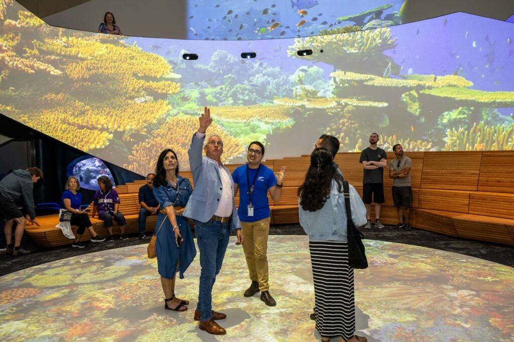 A small group of people standing in One Ocean Hall and looking up at the 360 degree projections surrounding them.