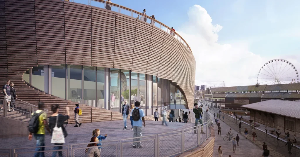 Rendering depicting the west exterior of the Seattle Aquarium's new Ocean Pavilion expansion, with crowds of people walking along the steps and walkways near the building on the waterfront.