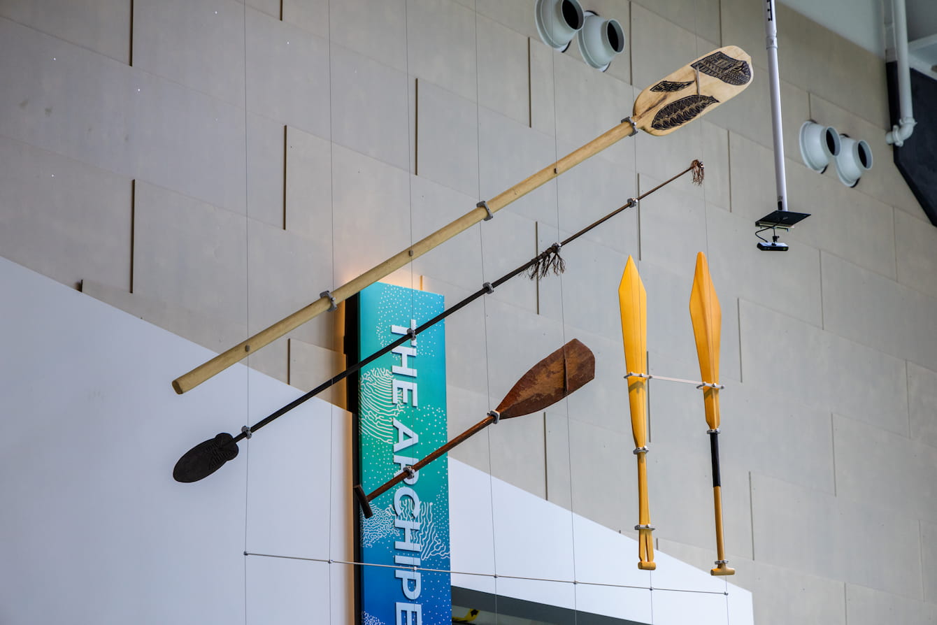 Five carved canoe paddles of varying shapes, lengths and textures hanging from the ceiling of the Ocean Pavilion.