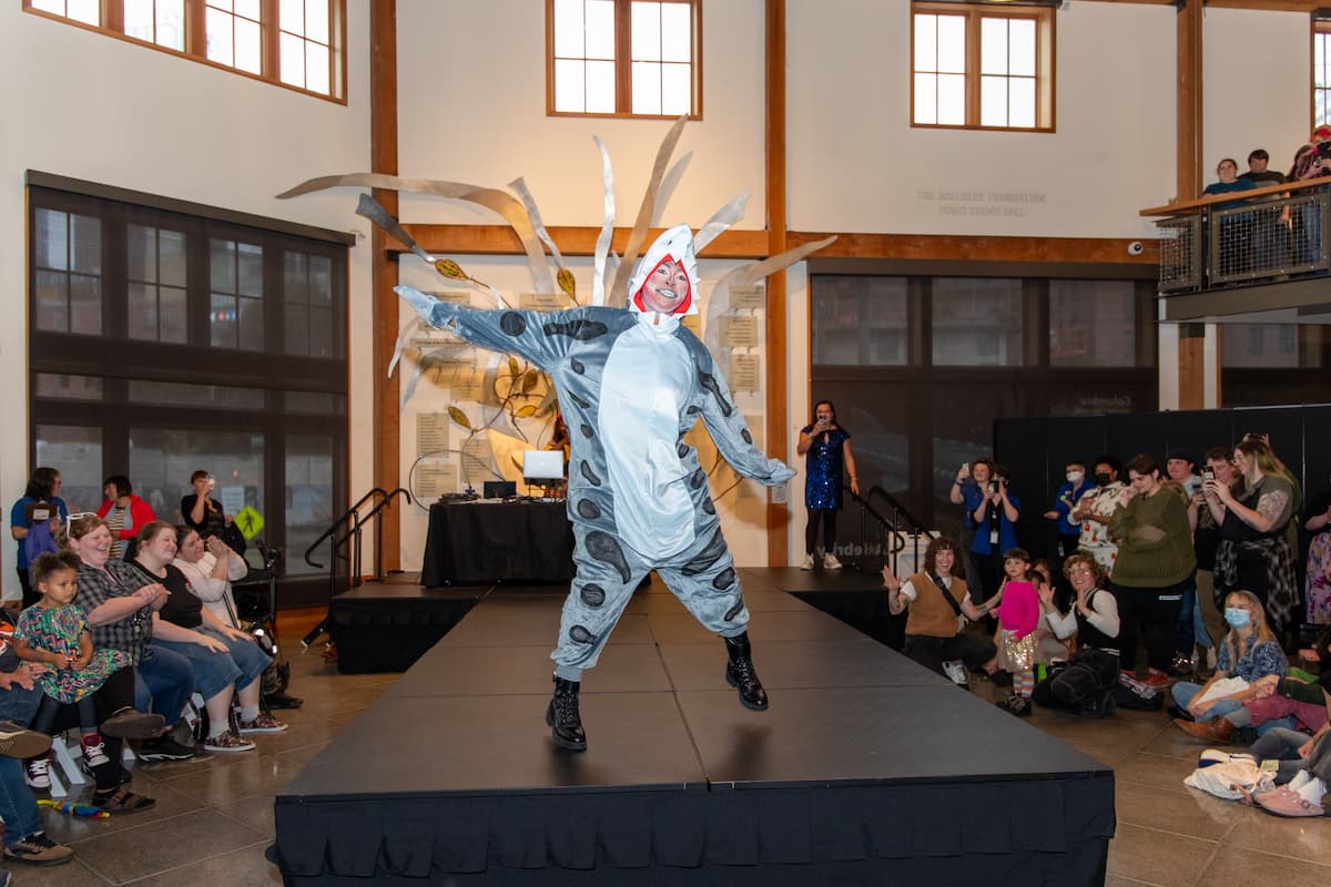 A performer in a shark costume and extravagant makeup dancing onstage.