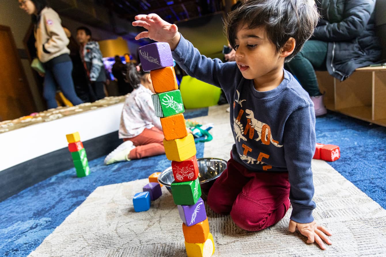 A child stacking colorful blocks on the floor.