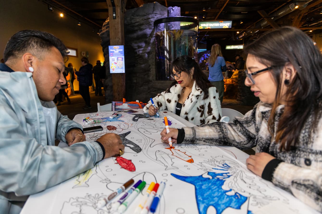 Three adults using markers to draw on a large coloring page.