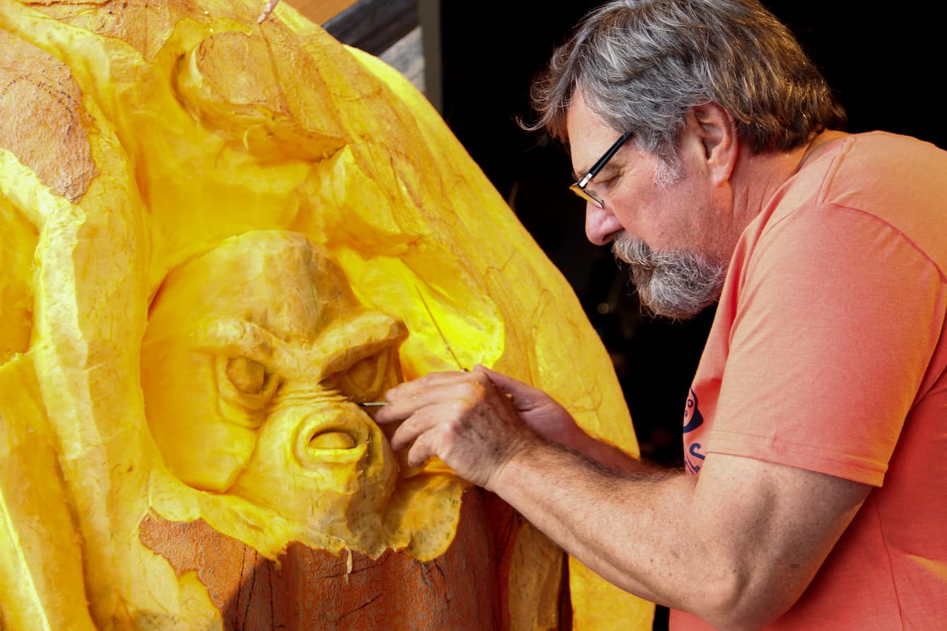 Russ Leno carving a giant pumpkin that stands about six feet tall.