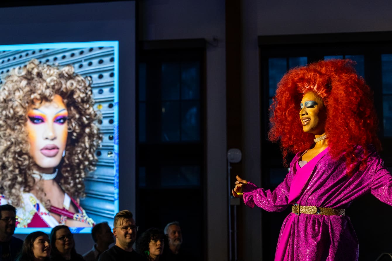 Drag queen Athena performing in a large, curly red wig and a purple robe.