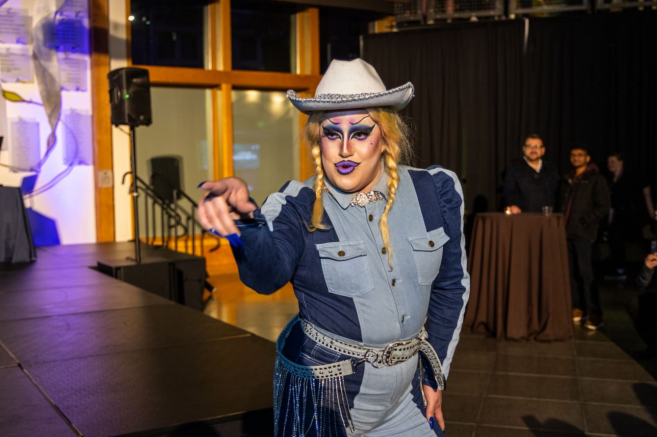 A drag queen in a blonde wig, white cowboy hat and denim jumpsuit performing at the Seattle Aquarium.