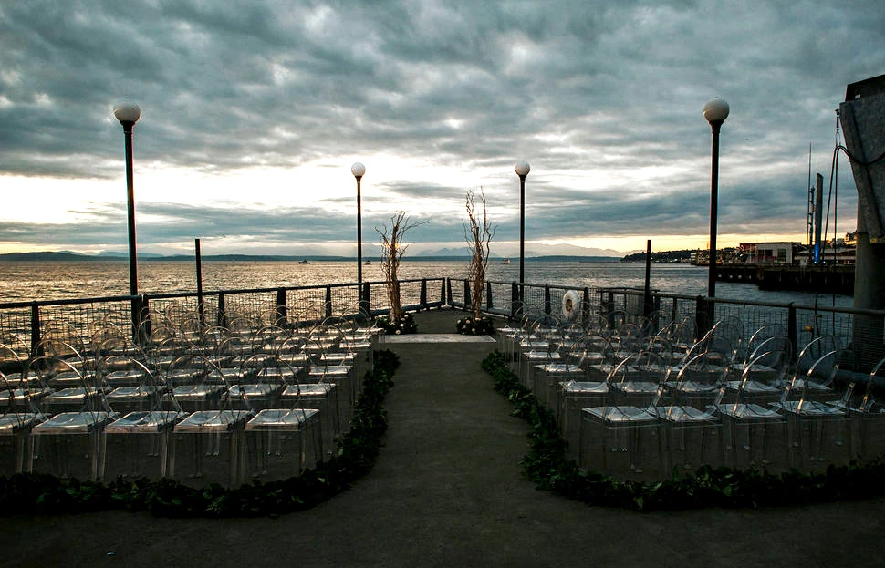 Chairs set up for a wedding ceremony facing two decorative pillars made of tree branches, against the backdrop of Elliot Bay from Seattle Aquarium's Pier 59.