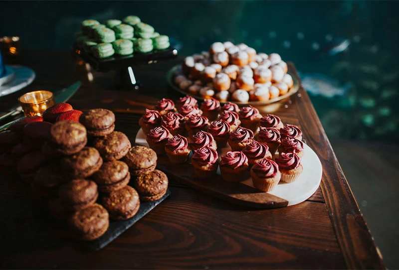 Cupcakes and assorted macarons placed and stacked on serving trays atop a wooden table.