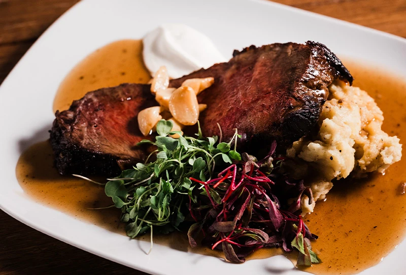 A slice of steak sitting on top of mashed potatoes, with a side of greens.